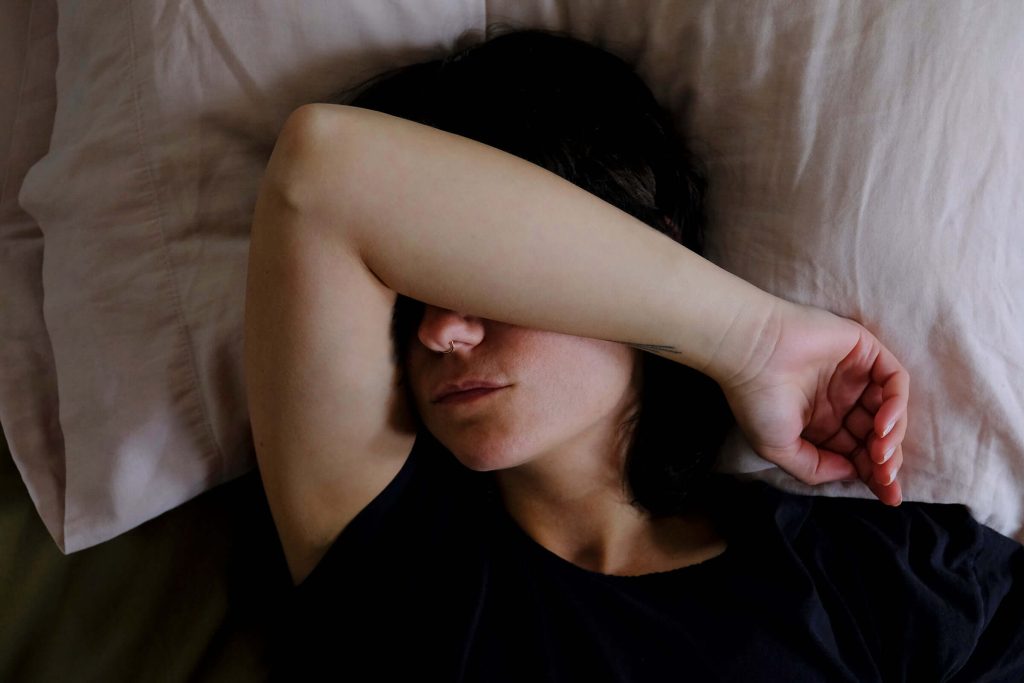 Woman laying down with arm over eyes, cant sleep