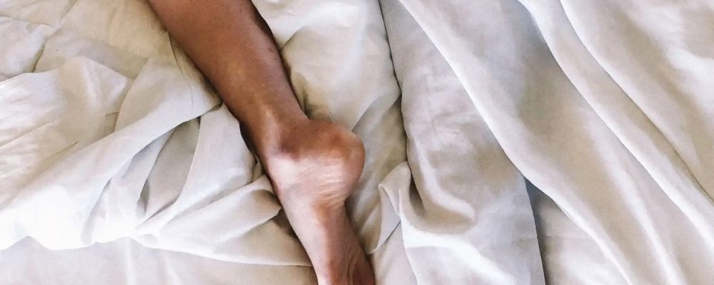 Depiction of Restless legs syndrome woman sleeping in white bedsheets with 1 leg out